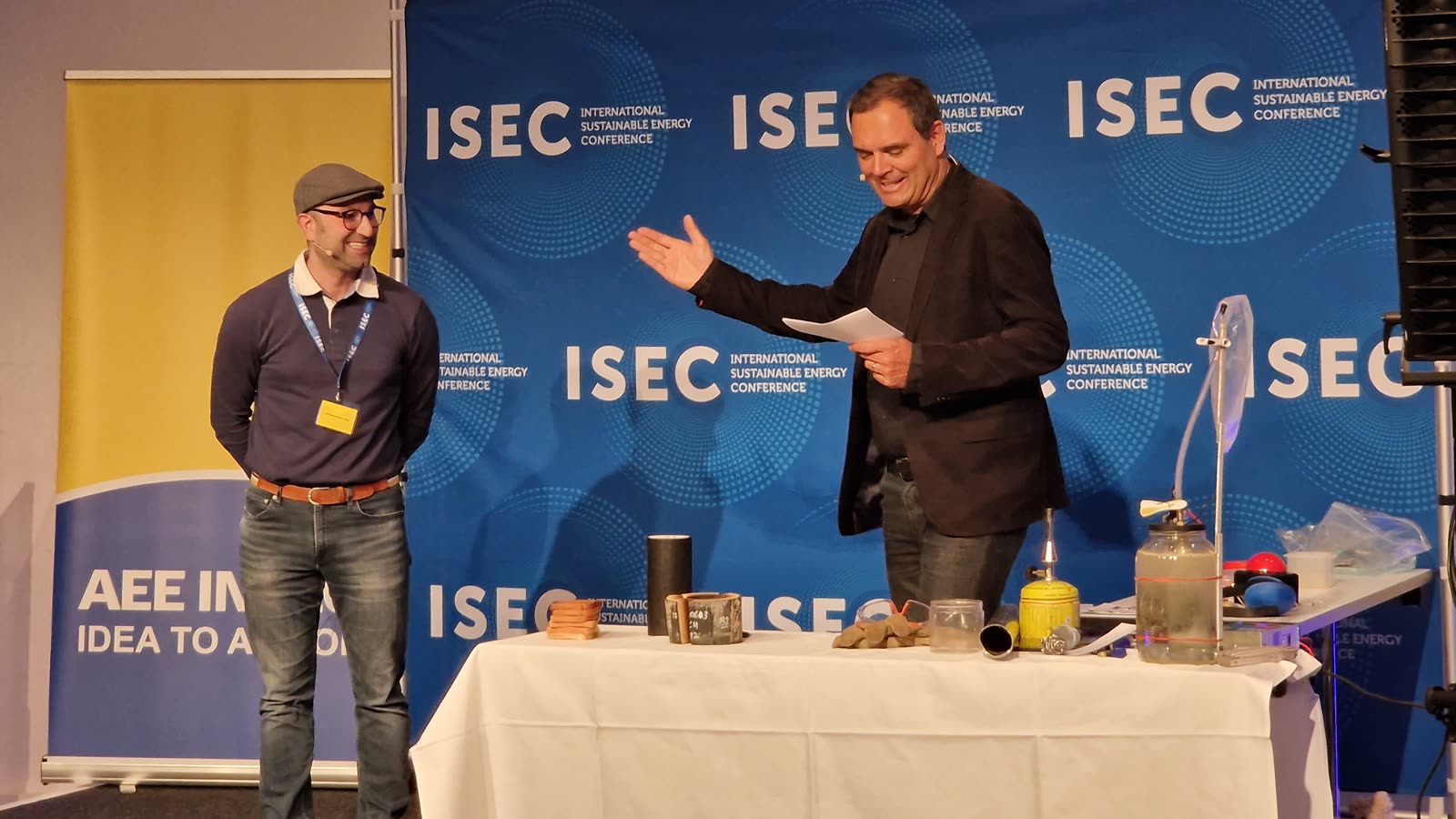 Pakdad Langroudi on stage at the Science SLAM, ISEC 2026 in Graz, beside a bench of demonstration apparatus